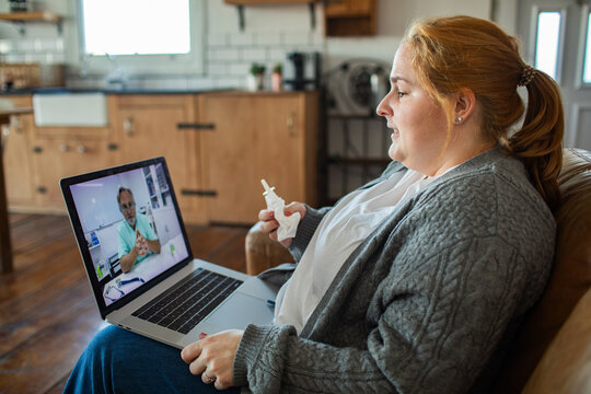 Woman holding nasal spray during online doctor consultation at home