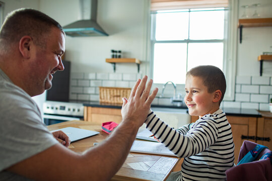Father and son high five during homework at kitchen table