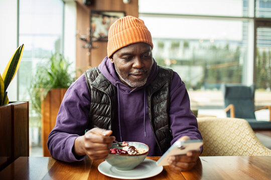 Senior man eating oatmeal and using smartphone at cafe