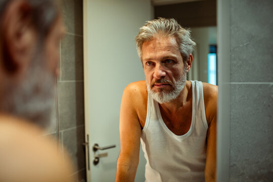 Middle-aged man looking at himself in bathroom mirror