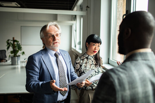 Business team discussing documents by window in modern office