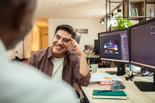 Smiling designer discussing project at dual monitors in modern office