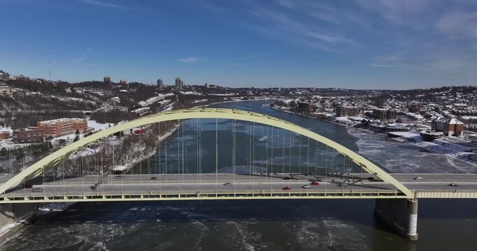 Aerial view of the yellow Daniel Carter Beard Bridge spanning the icy Ohio River with snow-covered banks and urban skyline in Cincinnati, Ohio, United States.