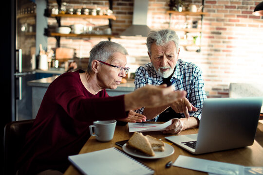 Senior couple reviewing household bills on laptop at home kitchen table
