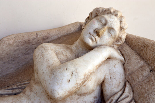 Dettaglio di una scultura classica in marmo raffigurante una figura dormiente o distesa, antico reperto archeologico romano di un coperchio di sarcofago