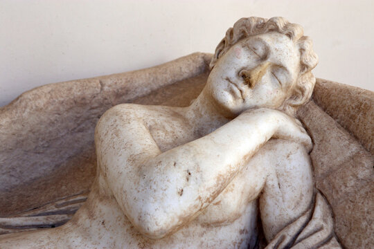 Dettaglio di una scultura classica in marmo raffigurante una figura dormiente o distesa, antico reperto archeologico romano di un coperchio di sarcofago