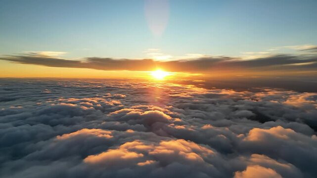 Aerial view of a golden sunrise over thick white clouds from a high altitude. The bright sun on the horizon illuminates the cloud tops with orange light and soft shadows at dawn.