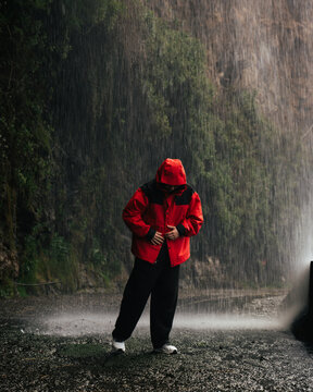 Man in red jacket standing under heavy rain in nature