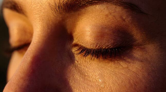 A close-up of a person's face with their eyes closed and a tear on their cheek