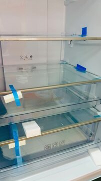 Closeup glass shelves refrigerator crisper compartment showing pristine clear drawers with blue protective tape, modern led