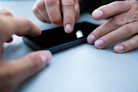 dettaglio delle mani di due uomini adulti mentre utilizzano e lavorano insieme ad un tavolo con uno smartphone