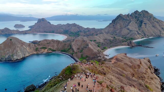 Aerial view of Komodo National Park featuring the iconic hills and bays of Padar Island with tourists gathered at the summit viewpoint in East Nusa Tenggara, Indonesia.