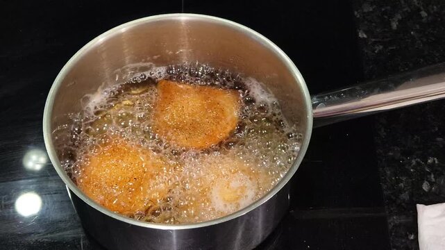 Portuguese rissois being fried in hot oil, a traditional appetizer cooking in a kitchen.