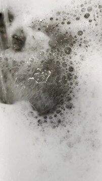 Water sprays onto thick soap suds in sink