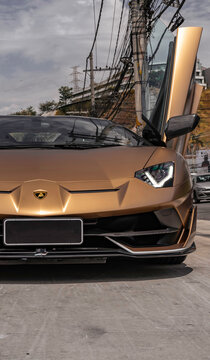 Matte bronze Lamborghini Aventador SVJ front view low angle with open doors, luxury sports car closeup in urban cenario
