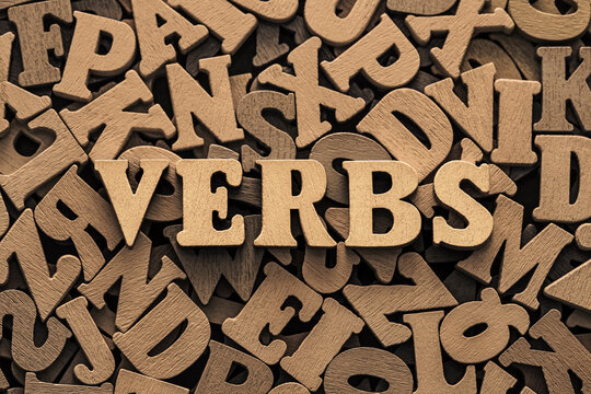 Inscription verbs on pile of old vintage wooden letters.

