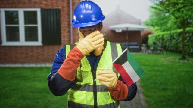 Man construction worker holding kuwait flag covering nose with gloved hand in building; duty concern.