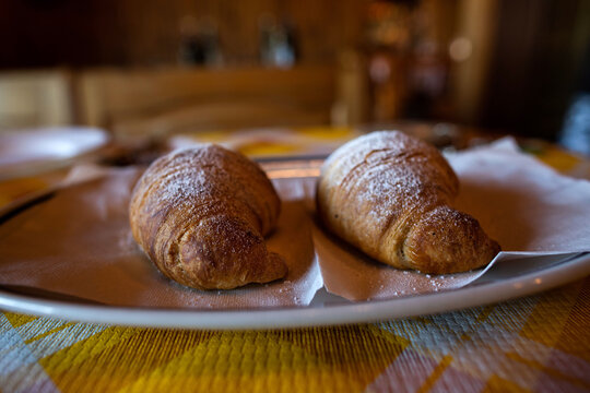 due brioche fresche, coperte con zucchero a velo, su un piatto, su un tavolo, al bar, per colazione