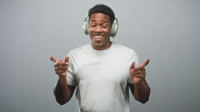 Man with headphones grinning and pointing fingers in gray studio setting with plain backdrop; joy groove.