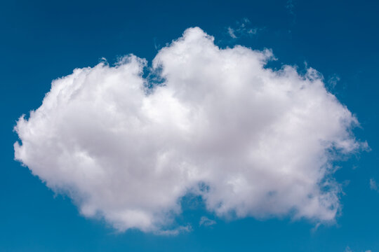 A single, fluffy white cumulus cloud floating isolated against a brilliant and clear deep blue sky background on a sunny day, showcasing beautiful natural textures and light.