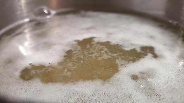 Close-up view of bubbling liquid in a stainless steel pot, showcasing the gradual formation of foam and texture in a cooking process over time