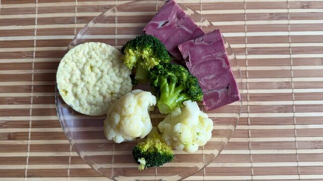 Light breakfast on glass plate broccoli. Boiled cauliflower paired with round rice white bread and two slices pork tongue