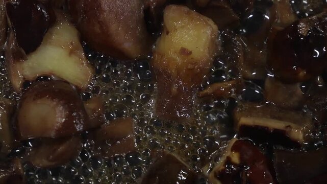 Chopped mushrooms frying in bubbling oil, showing gradual browning and caramelization in a frying pan, with visible bubbles and rich textures enhancing the cooking process