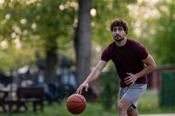 Fototapeta premium Young man dribbling basketball outdoors preparing for game