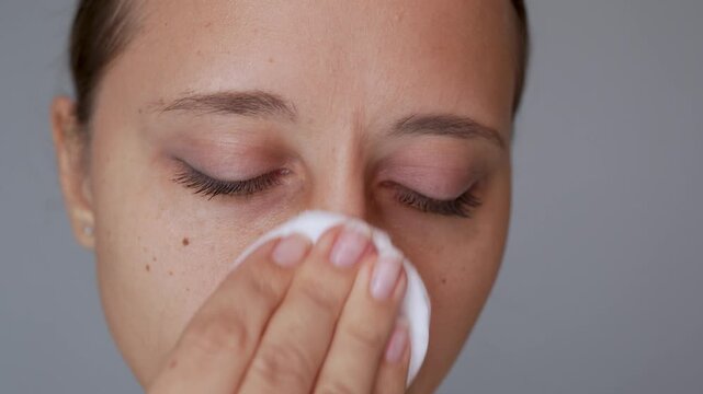 Close-up video of young woman gently wiping her cheek with cotton pad and micellar water. Facial cleansing, fresh skin and daily skincare routine concept
