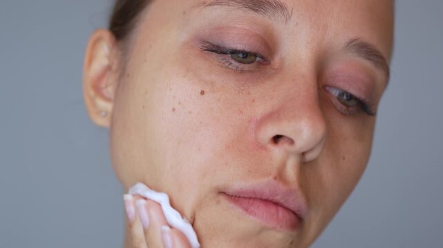 Young woman cleansing facial skin with cotton pad and micellar water. Gentle skincare routine, makeup removal and fresh clean skin concept