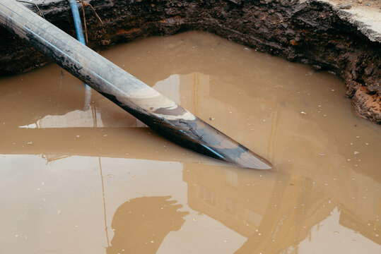 A shovel lies near the edge of an excavation site, partially submerged in muddy water. This scene captures the effects of recent rainfall on a construction area that is currently inactive