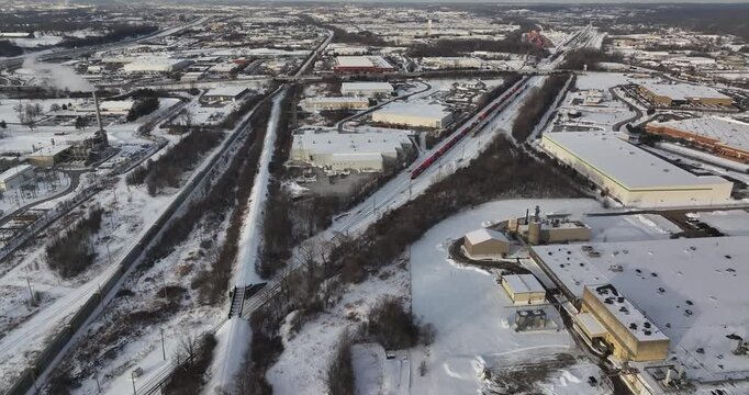 Aerial view of large industrial warehouses, a long red train on tracks, and a smoking chimney in a winter landscape covered in snow in Reading, Ohio, United States.