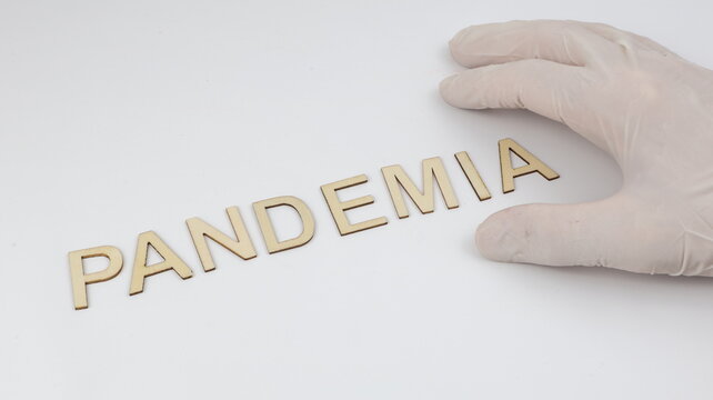 Pandemia scritta su legno. Una mano con un guanto di lattice tiene la scritta