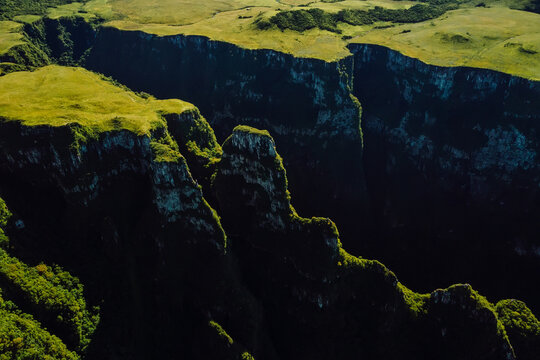 Dramatic drone view of deep canyon cliffs with green plateau and rugged landscape
