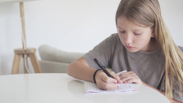 School-age girl writing letters in a workbook at home, focused on handwriting practice. Natural education video showing home learning, early literacy, schoolwork and a quiet KnowledgeForAll study