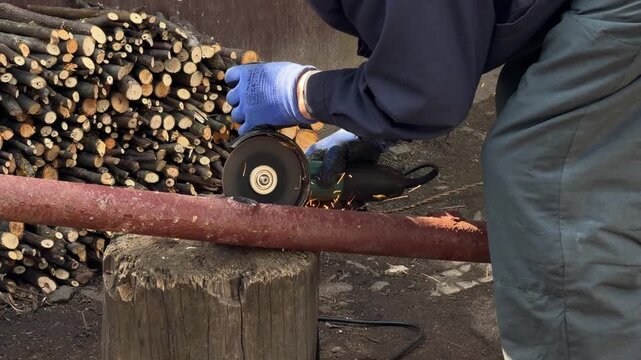 A skilled industrial worker uses an electric angle grinder to cut through a metal pipe outdoors, generating bright sparks during a professional construction and maintenance project