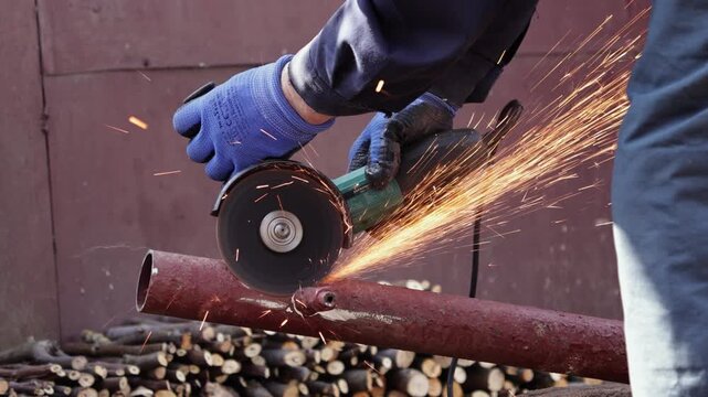 A professional construction worker uses a powerful electric angle grinder to cut through a metal pipe while creating bright orange sparks during industrial maintenance operations