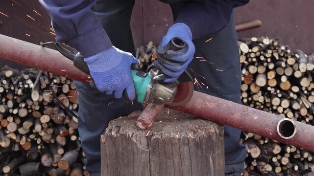 An industrial worker uses an angle grinder to cut a rusted metal pipe outdoors, generating bright sparks to showcase metal fabrication, construction site safety, and hardware skills