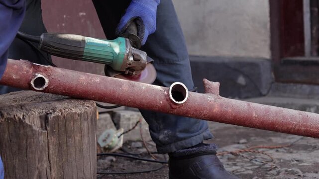 A dedicated worker uses an electric angle grinder to cut a rusty metal pipe, showcasing industrial maintenance, DIY construction, metalworking craftsmanship, and heavy-duty repair tasks