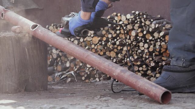 A dedicated worker uses an electric angle grinder to cut a rusty metal pipe in a backyard, illustrating manual labor and essential industrial maintenance for home improvement tasks