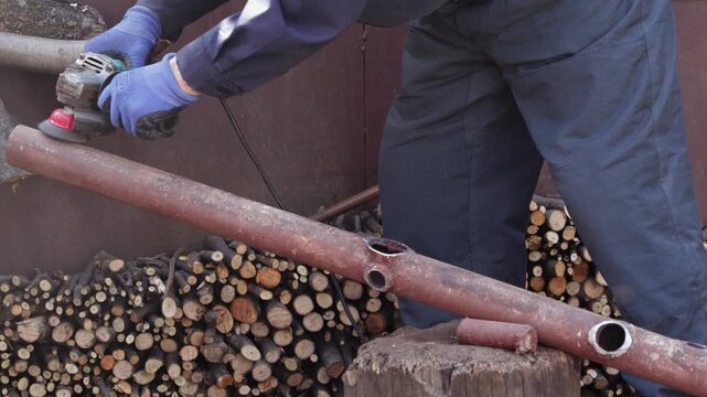 Worker using an angle grinder to smooth a metal pipe, focusing on precision industrial craftsmanship and repair work during a construction or DIY home renovation project outdoors