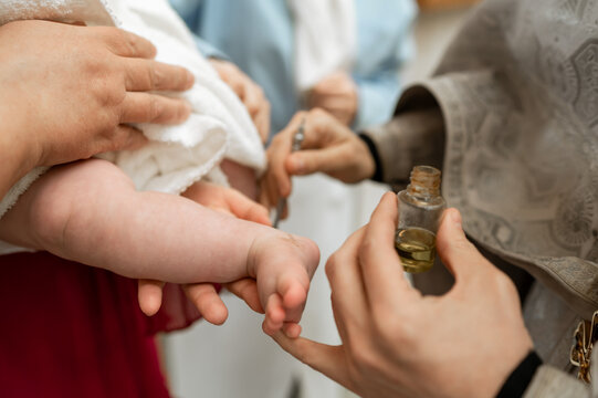 Priest anointing newborn baby foot with holy oil during Orthodox baptism ceremony in church