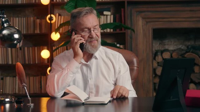 Caucasian senior elderly business man finishing writing notes answering mobile phone call taking frame with photo family grandchildren smiling talking old businessman male leader talk happy cheerful