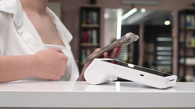 wireless payment terminal in beauty salon and woman paying for a service, contactless payment (NFC payment) using smartphone and plastic card