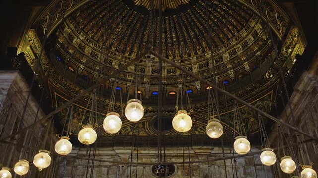 Slow motion 4K video of the magnificent interior dome of a historic mosque in Cairo, Egypt. The footage highlights glowing hanging lamps, intricate Islamic patterns, and rich architectural details ins
