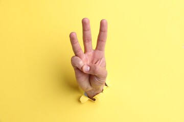 Obraz premium Man showing number three with fingers through hole in yellow paper, closeup