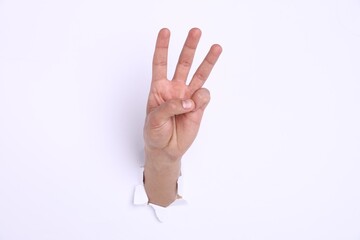 Obraz premium Man showing number three with fingers through hole in white paper, closeup