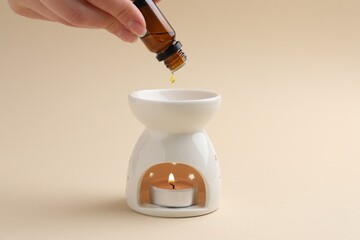 Obraz premium Aromatherapy. Woman dripping essential oil into aroma lamp on beige background, closeup