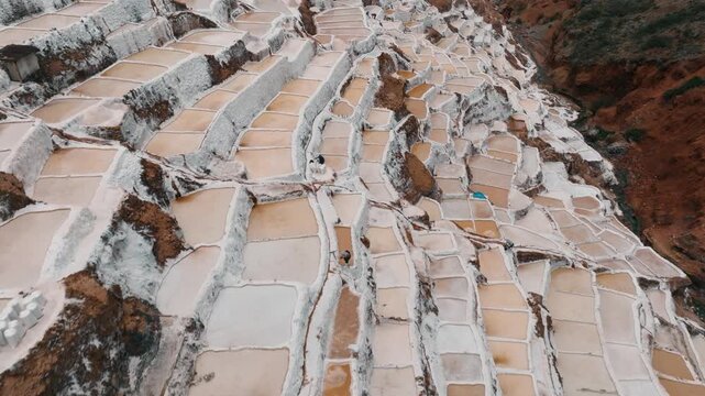 Drone aerial view of the historic Maras Salt Mines near Cusco, Peru. Thousands of terraced salt evaporation ponds cover the mountainside, creating a striking geometric pattern in the heart of the Sacr