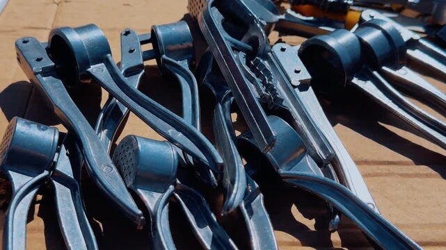 Close-up garlic presses at flea market showing new stainless squeezers arranged on wooden table, sunlight glinting off metal